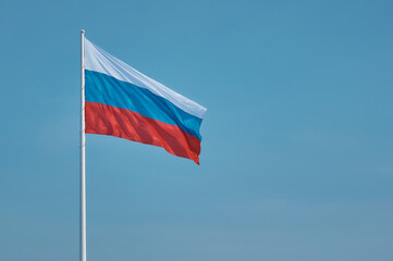 Flag of Russia against the blue sky. High flagpole on the embankment of the city of Blagoveshchensk, Russia. The tricolor cloth moves smoothly in the wind. Room for text.
