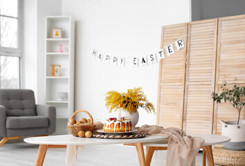 Easter cake, basket with eggs and mimosa flowers on table in room