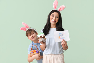 Little boy, his mother with greeting card, Easter cake and eggs on green background