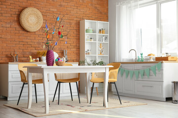 Vase with tree branches and basket of Easter eggs on table in stylish room interior