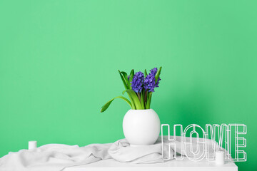 Vase with beautiful flowers and word HOME on table near color wall