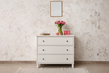 Vase with tulips, books, eyeglasses, candle and cube calendar on chest of drawers near light wall in room interior