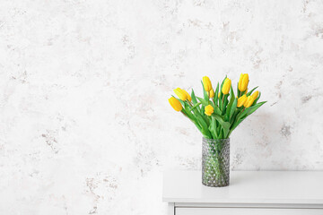 Vase with beautiful tulips on chest of drawers near grunge wall