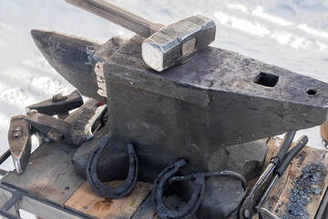 On an old iron anvil lies a blacksmith's working hammer. The working machine is standing on the snow on the street near the workshop. 