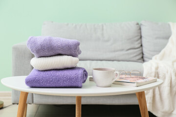 Stack of knitted sweaters and cup on table in room