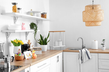 Vase with tulips, Easter eggs, greeting card and stylish decor on counter in kitchen interior