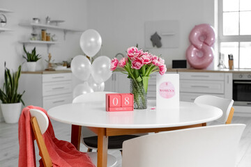 Cube calendar, tulips and greeting card with text HAPPY WOMEN'S DAY on dining table in kitchen