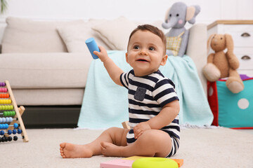 Cute baby boy playing with toys on floor at home