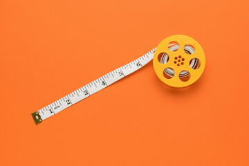 Diagonally unwound measuring tape on an orange background. Flat lay.