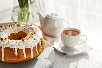 Board with tasty Easter cake and cup of tea on light table