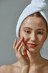 Redhead young girl putting moisturizing cream on face with freckles for healthy skin around eyes. Skincare cosmetics ad