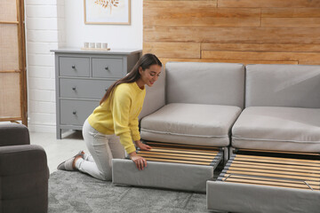 Young woman unfolding sofa into a bed in room. Modern interior