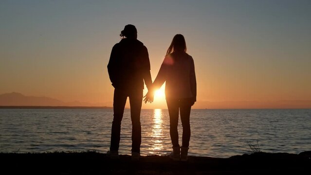 Silhouette of loving couple holding hands against sunset.