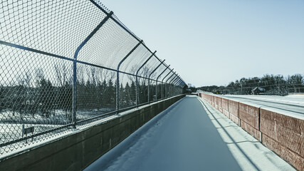 Sidewalk over the highway covered in snow with chain-link fence and concrete barricade