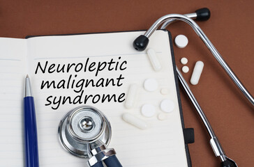 On a brown surface lie pills, a pen, a stethoscope and a notebook with the inscription - Neuroleptic malignant syndrome