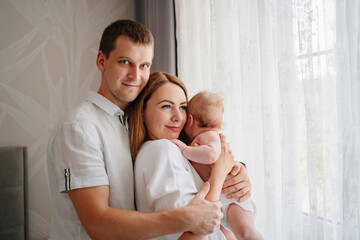 a happy family with a newborn baby by the window. mom, dad and baby.