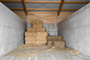 Yellow dry haystacks in square shape stand on top of each other in concrete shed for feeding cattle...