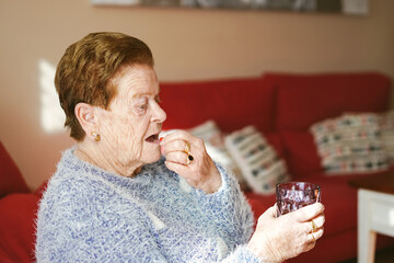 an elderly Caucasian woman takes a medicine pill while holding a glass of water
