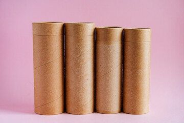 Packing cardboard tube made of kraft paper. Cardboard cylindrical packages stand on a pink...