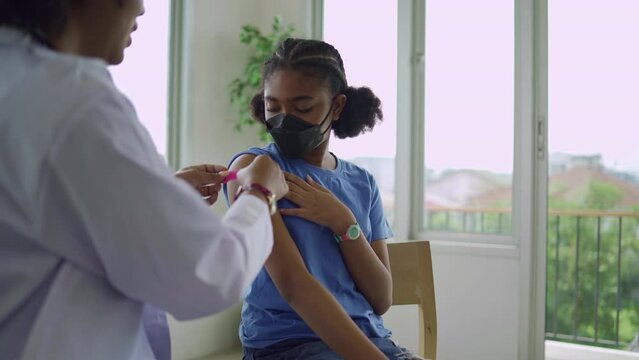 A female doctor is applying plaster to a child's shoulder after being vaccinated. Children wear face masks. Opening sleeves to vaccinate against flu or epidemic in health care and vaccinated concept