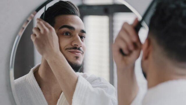 Arabian spaniard arab man looking at mirror combing hair with hairbrush getting ready in bathroom home guy morning beauty routine in bath mirror reflection styling haircut stylish preparing for dating