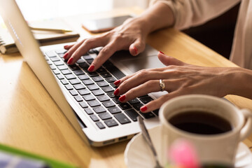 women's hands writing on a laptop, coffee and cell phone on a wooden table