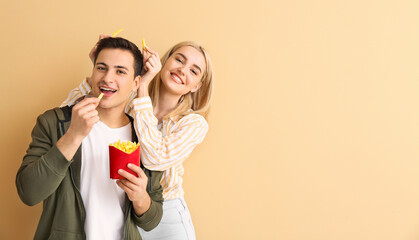 Happy young couple with french fries on beige background