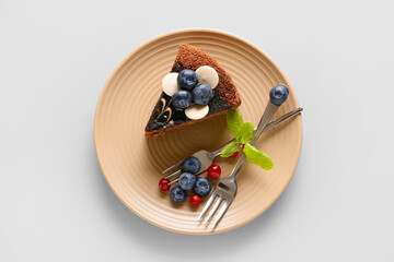 Plate with delicious piece of chocolate cake and berries on light background