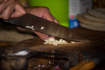hand with a knife cutting garlic on wood, background food