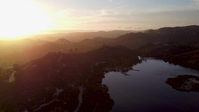 A beautiful aerial shot flying over the mountains of Dixon Lake with crystal clear water during golden hour in Escondido, California