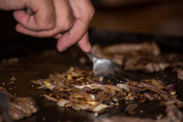 hand sautéing onion on iron griddle