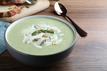 Delicious asparagus soup with pumpkin seeds served on wooden table, closeup