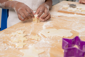 Kids in white aprons cutting figures in rolled dough while making tasty cookies for holiday