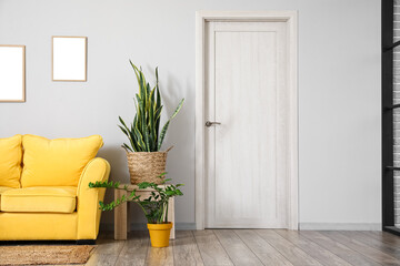 Wooden table with houseplants and yellow sofa near light wall