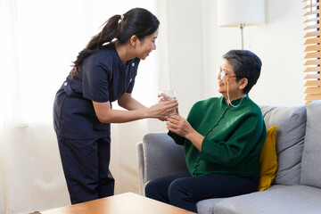 Obraz premium Smiling nurse giving glass of water to senior asian woman in nursing home or assisted living facility.