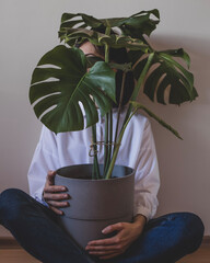 Young woman is sitting with a big flower pot with monstera