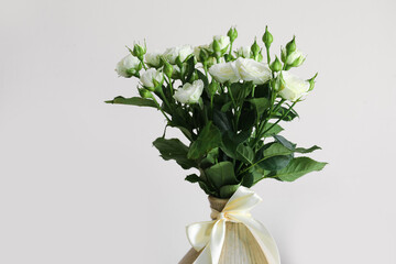 Vase with bouquet of beautiful fresh roses near light wall