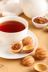 Obraz na płótnie Canvas Tasty walnut shaped cookies with boiled condensed milk and cup of tea on beige background