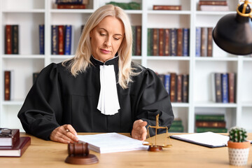 Mature female judge working with documents at table in courtroom
