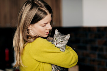 Young woman in home clothes hugging her cat at home