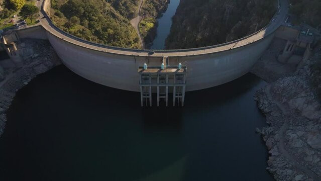 4K aerial view of a Portuguese water dam. Flying above the Barragem do Cabril, drone moving forward and tipping down revealing the massive rounded concrete wall of the dam. 60fps