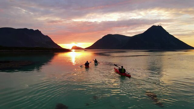 Aerial drone view following kayaks, paddling towards mountains and the sunset in Lofoten, Norway