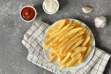 Plate with tasty french fries and sauces on grey background