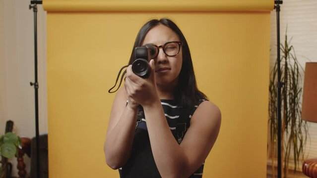 Young Asian woman in a studio brings a super8 film camera up to her face