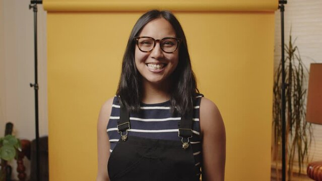 Happy Asian woman gestures frame lines in a studio with a yellow backdrop