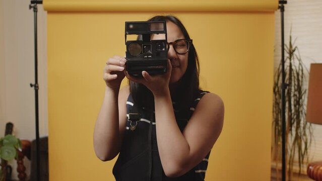 Young Asian woman in home studio holds up a polaroid camera and takes a picture
