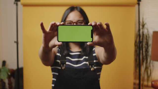 Young Asian woman lifts her mobile phone to display a landscape greenscreen smartphone