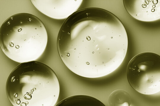 Skin care serum gel texture, oil drops on green background. Cosmetic product swatch with bubbles macro