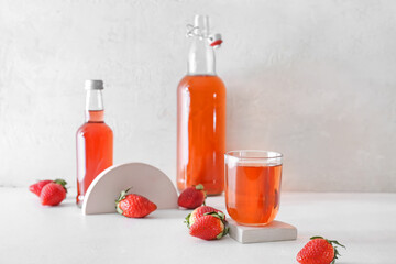 Bottles and glass of fresh strawberry kombucha on light background