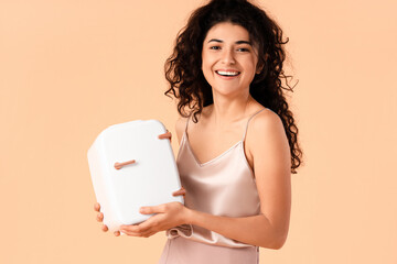 Young smiling woman holding cosmetic refrigerator on color background